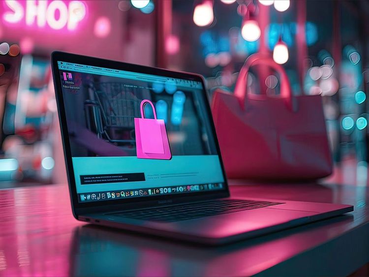 Laptop auf Tisch mit geöffneter Webseite, die eine pinkfarbene Einkaufstasche auf dunklem Hintergrund zeigt, unscharfe pinkfarbene Tasche im Hintergrund.